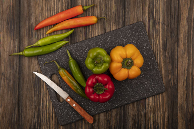 胡椒新鲜辣椒的顶视图在一个黑色的厨房板上用刀与辣椒隔离在一个木墙上景观辛辣顶部