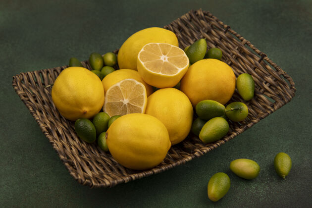 块柳条托盘上黄色柠檬的俯视图 绿色墙壁上孤立着金盏花托盘柠檬新鲜