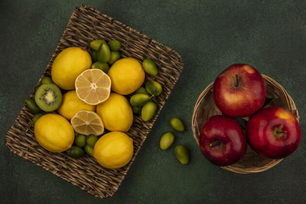 片黄色柠檬放在柳条托盘上的俯视图 绿色墙上的桶上放着金盏花和红苹果桶柑橘配料