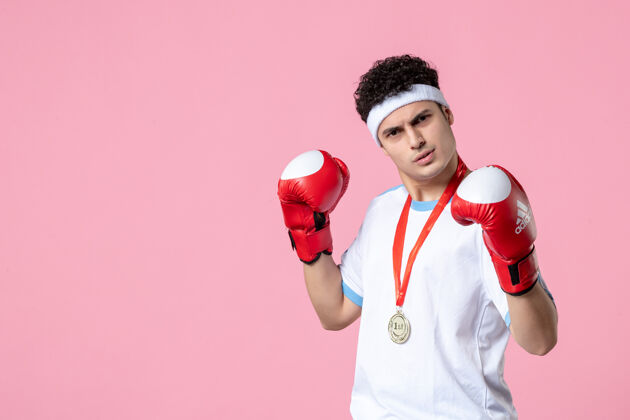 手套正面图年轻的男拳击手穿着运动服 戴着拳击手套站在粉红色的墙上盒子专业成功