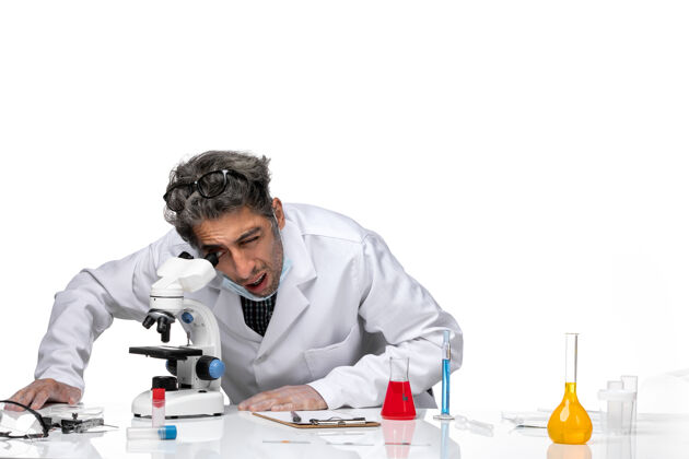 显微镜前视图中年科学家穿着特殊的白色西装使用显微镜外套专业人