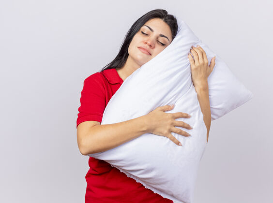 年轻昏昏欲睡的年轻白人病女孩抱着枕头把头枕在上面 闭着眼睛 隔离在白色背景上 留着复印空间眼睛疾病枕头