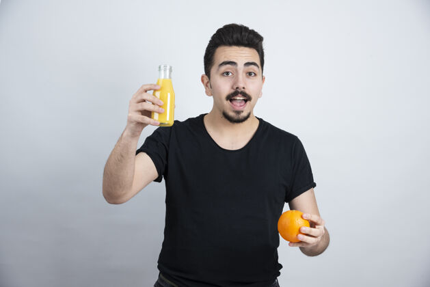 休闲留着胡子的男人拿着橘子和玻璃瓶果汁时尚肖像男孩