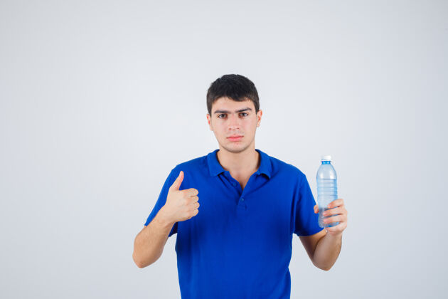 男孩年轻人拿着塑料瓶 在t恤衫上竖起大拇指 看起来很自信 正前方视图青少年表情拇指
