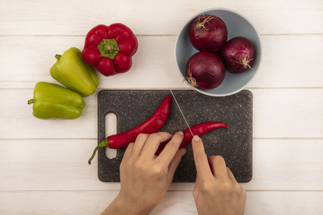 食物俯视图中的女性手切辣椒在黑色的厨房板上用刀在白色的木墙上辣椒顶部切割