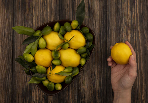柠檬顶视图中的女性手拿着一个柠檬和一碗柠檬和金盏花在木墙上厨房视图食物