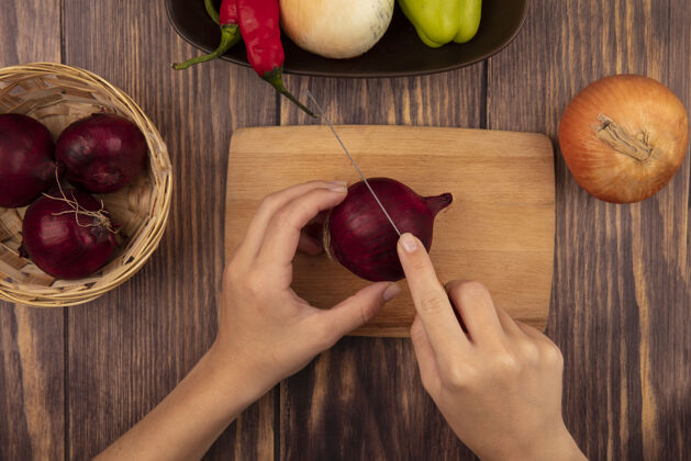 特写俯视图中的女性手切割一个新鲜的红洋葱在木制厨房板上用刀在木墙上食物薯条桌子