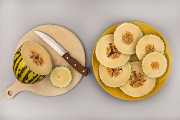 厨房顶视图新鲜的哈密瓜在一个木制的菜板上用刀与瓜片在一个黄色的盘子在白色的墙上顶部食物切片