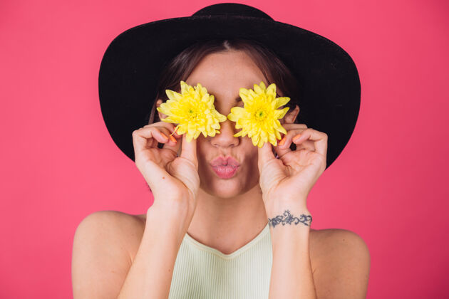 女性时尚女人戴着帽子 送上飞吻用黄色紫苑遮住双眼 春意盎然 快乐情感与世隔绝的空间自然植物学人