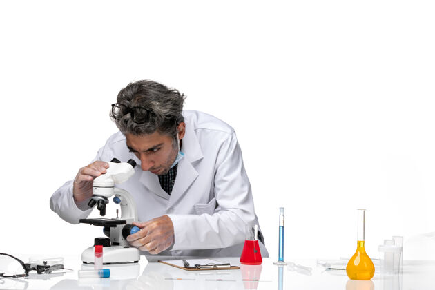 医学前视图中年科学家穿着特殊的白色西装使用显微镜视图使用外套