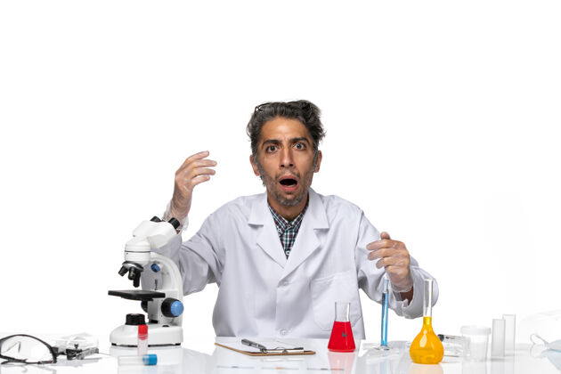 病毒前视图穿着医疗服的中年科学家围坐在桌子旁 拿着解决方案实验技师坐姿