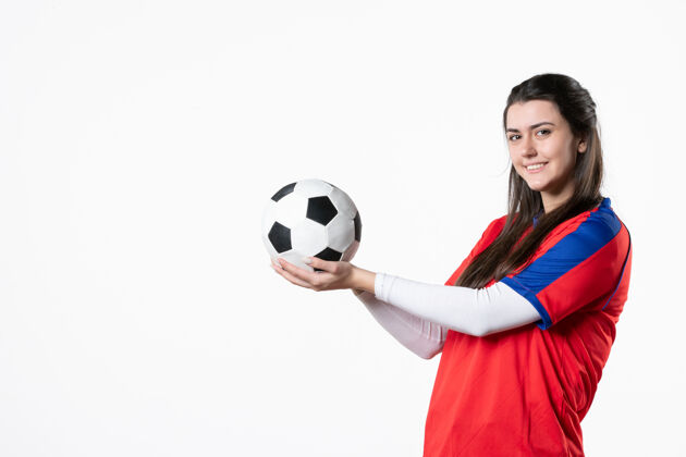 年轻女性前视图穿着运动服的年轻女性 白色墙壁上有足球足球游戏球