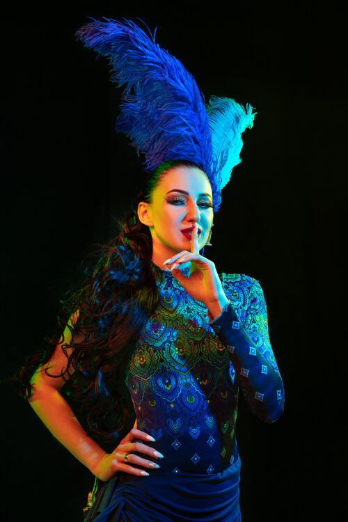魅力美丽的年轻女子在嘉年华 时尚的化装服装与羽毛的黑色背景在霓虹灯下模特女性服装