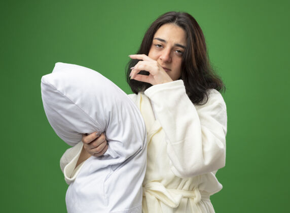 侧面体弱多病的年轻白人女孩穿着长袍站在侧视图拥抱枕头看着相机保持手在空气中隔离绿色背景长袍拥抱绿色