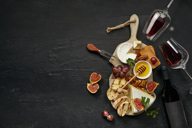 红色两杯红酒和一个美味的奶酪盘子 上面放着水果 葡萄 坚果和烤面包 放在黑色石头背景的木制厨房盘子上奶酪味道厨房