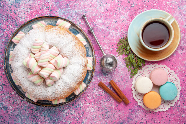 生的粉红色表面上有一杯茶和麦卡龙的糖粉蛋糕俯视图饼干勺子杯子