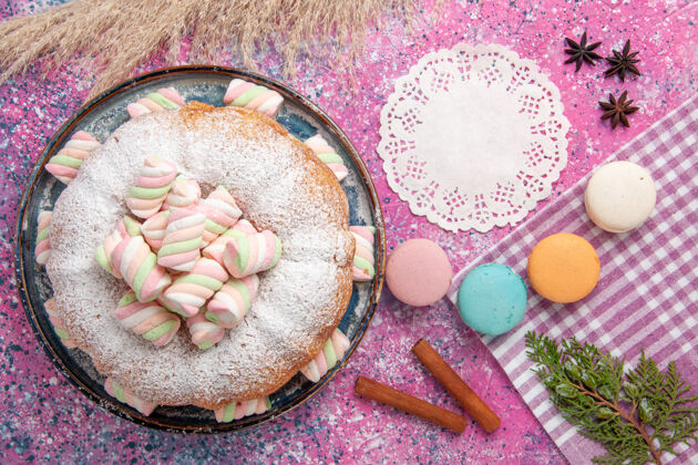 饼干粉红色表面上有麦卡龙和棉花糖的糖粉蛋糕俯视图美味健康顶视图