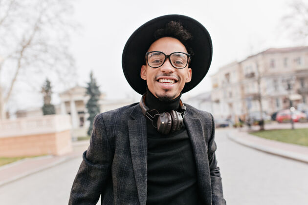 时尚笑脸非洲男子 时尚卷发 头戴帽子黑皮肤男模特的户外照片 在探索城镇时玩得很开心非洲帽子散步