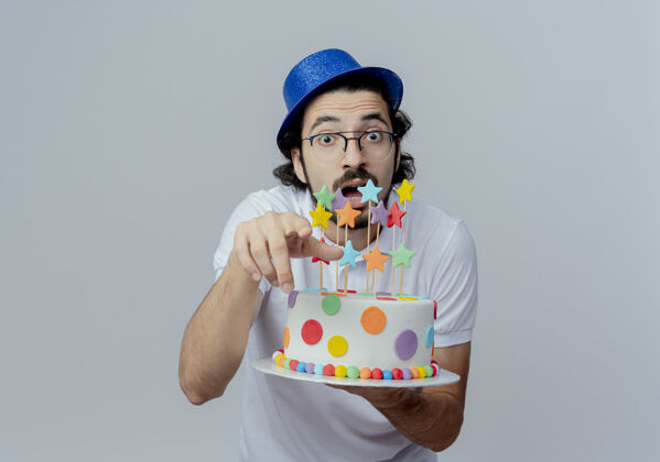 拿着惊讶的帅哥戴着眼镜 戴着蓝色的帽子 手里拿着蛋糕 向你展示着孤立在白色上的手势惊喜帽子戴着