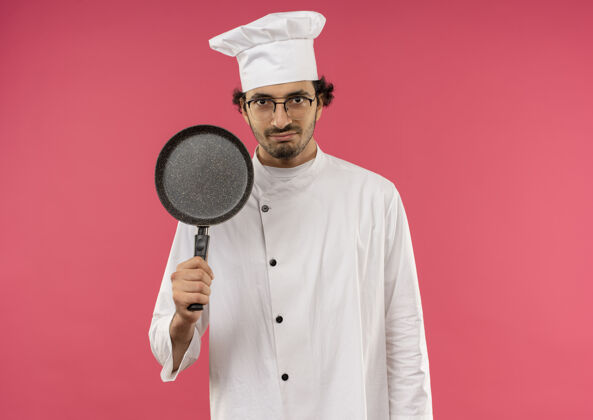 男年轻的男厨师穿着厨师制服 戴着粉红色的玻璃杯 手里拿着平底锅粉色请平底锅