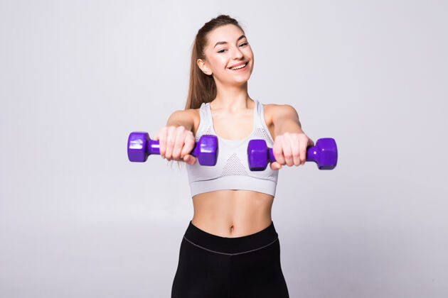 力量健康的女人 带着哑铃在白墙上锻炼健身馆的概念设备欢呼强壮