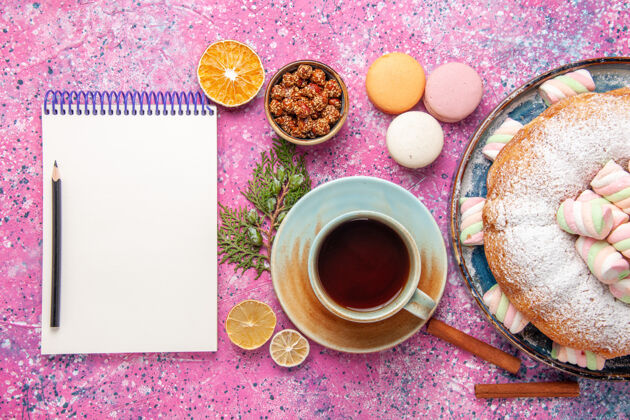 美味粉红色表面上有一杯茶和法式马卡龙的糖粉蛋糕俯视图茶碟食物法国