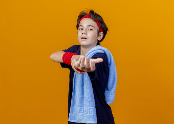 腕带年轻帅气的运动男孩戴着头带和护腕 肩上戴着牙套和毛巾 站在橙色的墙上孤立的侧视图里衣服表情姿势