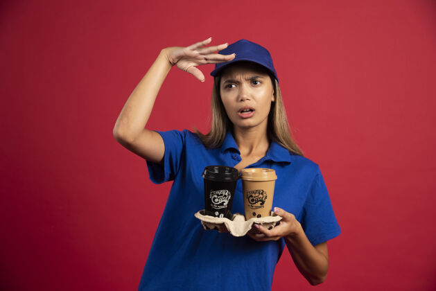 咖啡穿着蓝色制服的年轻女子手里拿着一盒两个杯子人女士帽子