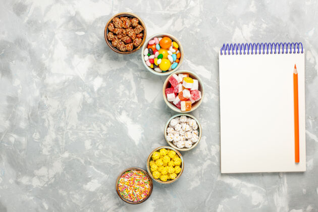 糖果白色表面上有棉花糖和记事本的不同甜糖果的俯视图五颜六色棉花糖食物