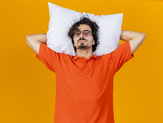 眼镜虚弱的年轻病患戴着眼镜抱着枕头在头下看着前面隔离在橙色墙上姿势穿着站着