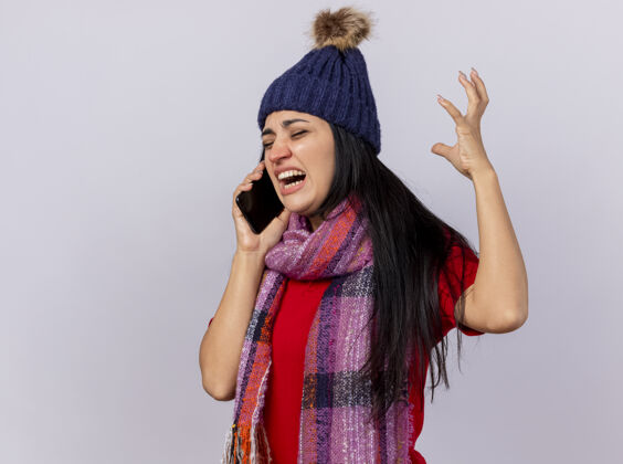 公民愤怒的年轻生病的女人戴着冬天的帽子和围巾站在侧视图上讲电话保持手在空中闭着眼睛隔离在白墙上帽子女人围巾