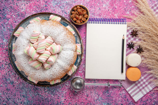 粉糖粉蛋糕的俯视图 浅粉色表面上有麦卡龙和记事本美味麦卡龙含糖