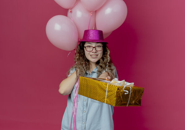 粉色微笑的年轻女孩戴着眼镜 戴着粉红色的帽子 手里拿着纳洛恩 手里拿着礼盒 对着镜头孤立的粉红色戴着帽子眼镜