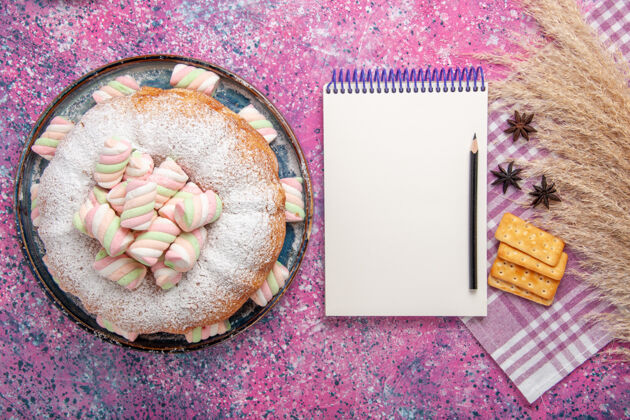 记事本粉红色表面上有饼干和记事本的糖粉蛋糕俯视图美味顶视图相框