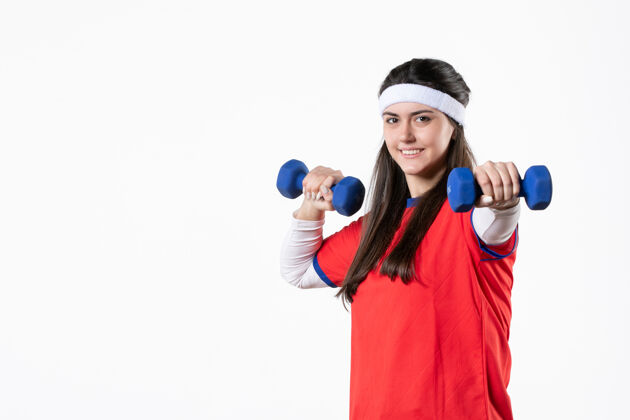 视图正面图：穿着运动服 戴着蓝色哑铃的快乐年轻女性人青少年球员