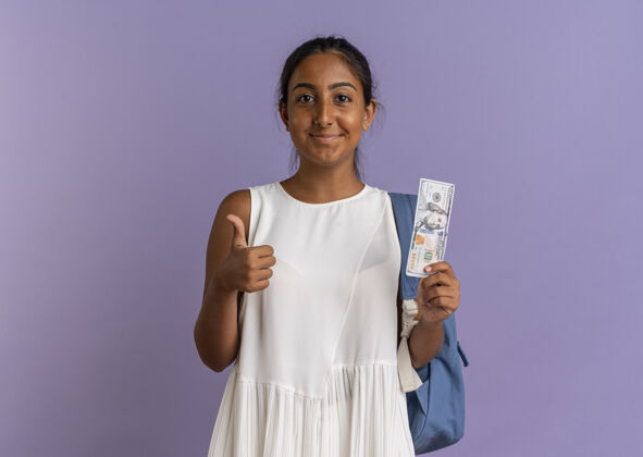女学生高兴的年轻女学生戴着背袋拿着钱 她的大拇指在紫色上紫色向上包