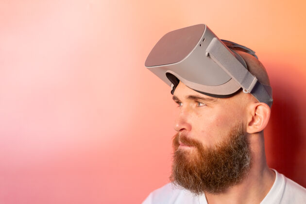 活动一个留着胡子的男人在工作室里戴着虚拟现实眼镜 背景是粉橙色的 这是一幅感人的肖像视觉成人设备