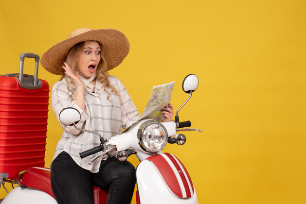 摩托车顶视图年轻女子戴着帽子 坐在摩托车上 看着地图感到惊讶的黄色年轻女子坐感觉