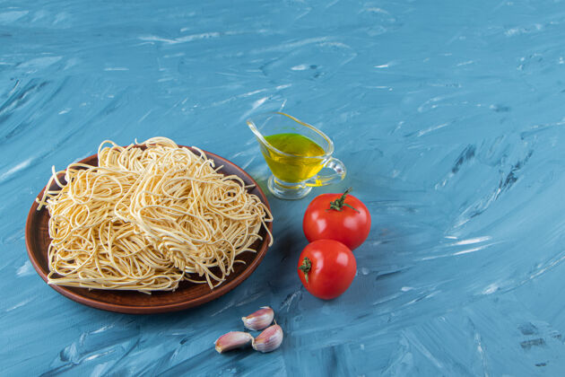 意大利面一盘棕色的生面条 两个新鲜的红色西红柿和油 蓝色背景一餐意大利面营养