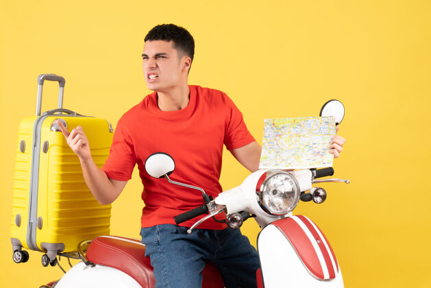 身体正面图愤怒的年轻人穿着休闲服 手持旅游地图骑在轻便摩托车上抱着旅行人