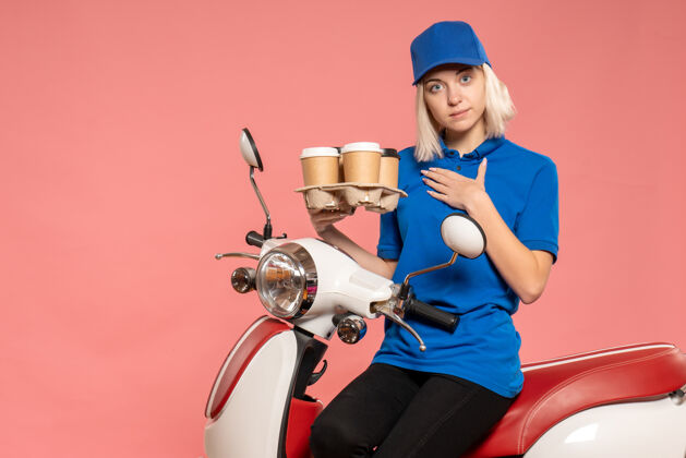 肖像正面图骑自行车的女快递员 咖啡杯是粉红色的杯子摩托车送货