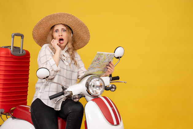 举行戴着帽子坐在摩托车上拿着地图的年轻女子对黄色感到惊讶人微笑脸