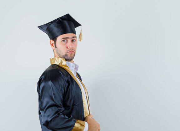 男人年轻的男性拿着他的毕业制服礼服 看起来很严肃前视图礼服男人男人