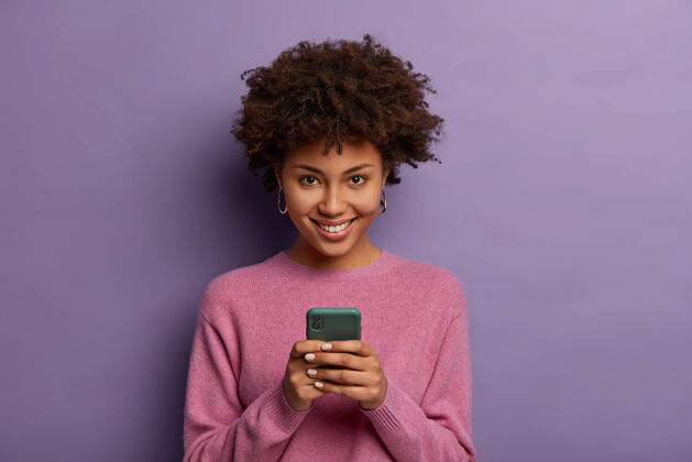 沟通可爱的少数民族妇女肖像手持现代手机 使用电子设备上网 神采奕奕 连接无线互联网 穿着休闲毛衣 在室内摆姿势姿势年轻女人