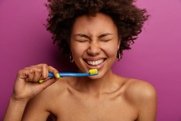 口腔日常生活 晨练和洁牙理念赤膊上阵黑皮肤女人用牙刷刷牙 赤裸着站在紫色墙壁上 心情很好女士牙齿女孩