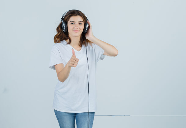 女人年轻女性在欣赏音乐时竖起大拇指 头戴耳机 穿着白色t恤 牛仔裤 看上去很开心正面图快乐模特女性