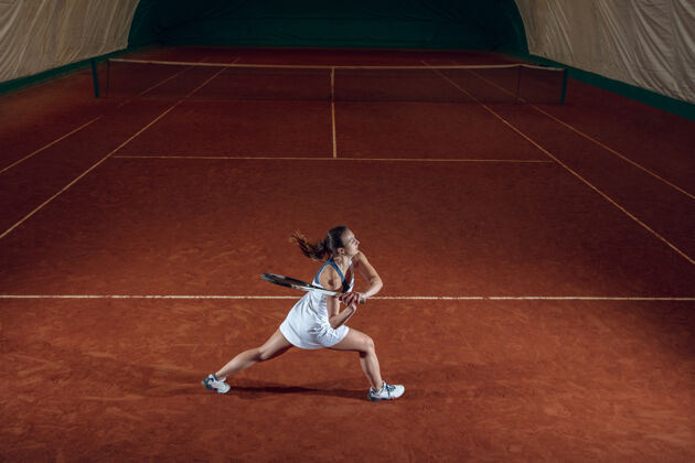 年轻年轻的职业女运动员在运动场的墙上打网球设置专业手电筒