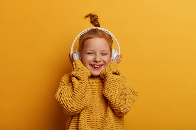 模型科技 孩子 音乐概念漂亮的微笑着的姜黄色头发的小孩戴着立体声耳机 享受纯净的声音 听最喜欢的歌 开心地笑 穿着针织毛衣结高兴休闲