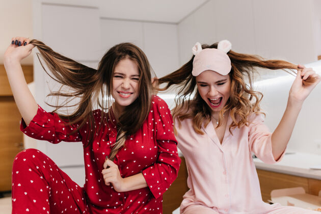 成人穿着粉色睡衣的优雅女孩在玩她的卷发一大早漂亮的姐妹们在室内嬉戏的画像漂亮微笑卧室
