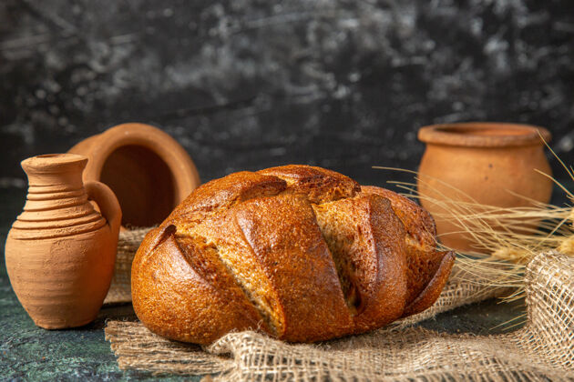 烘焙一条棕色毛巾上的食用黑面包和深色表面上的陶器的俯视图面包条食品视野